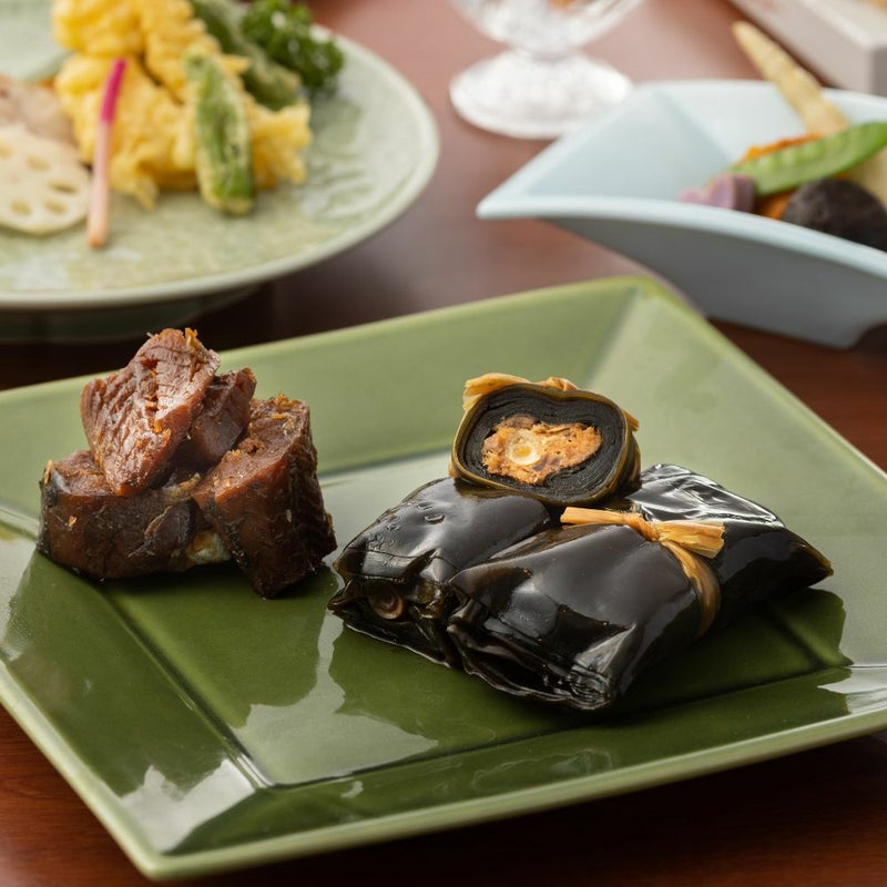 うま煮数種類がカットされお皿に盛りつけられ、その他のおかずと並んだ食卓イメージの画像です。